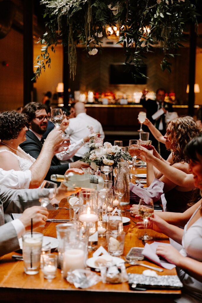 A bride and groom raise their glasses with members of their wedding party at their table during their wedding reception