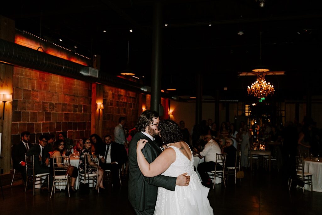 A bride and groom share their first dance together while guests of their indoor wedding reception at The Atrium in Milwaukee watch