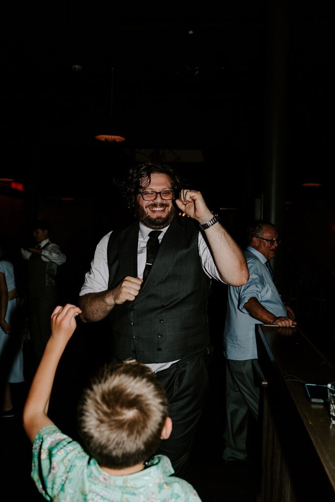 A groom smiles and lifts a fist in the air while a child in front of him does the same