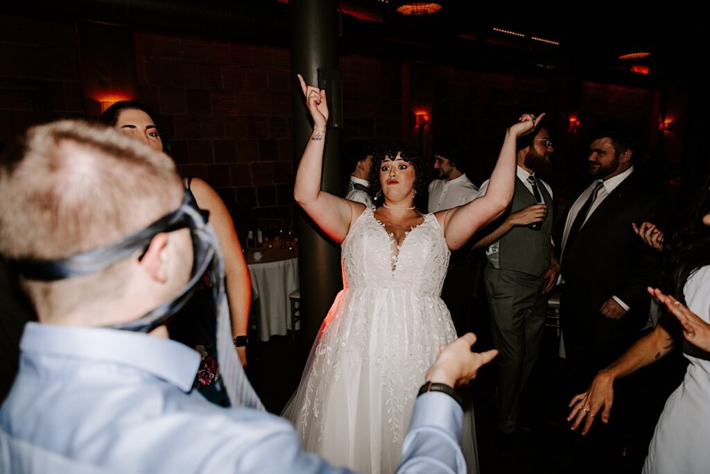 A bride gestures towards the air while dancing during her indoor wedding reception at The Atrium in Milwaukee