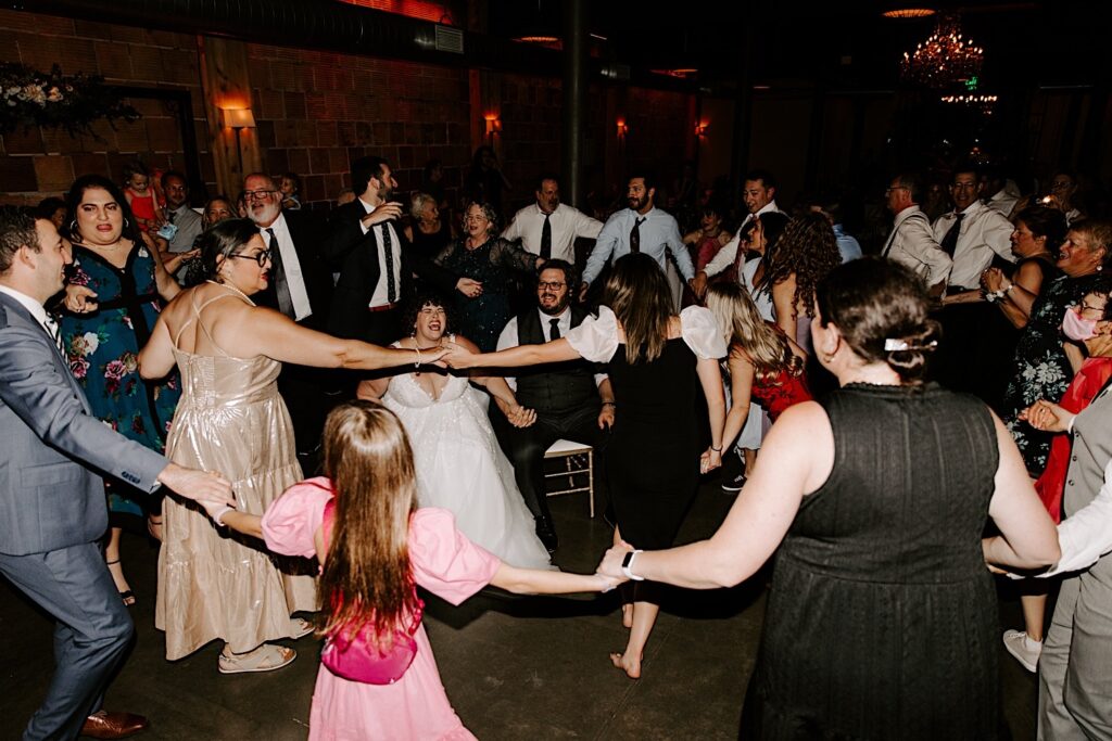 A bride and groom sit in the middle of a dance circle during their indoor wedding reception at The Atrium in Milwaukee