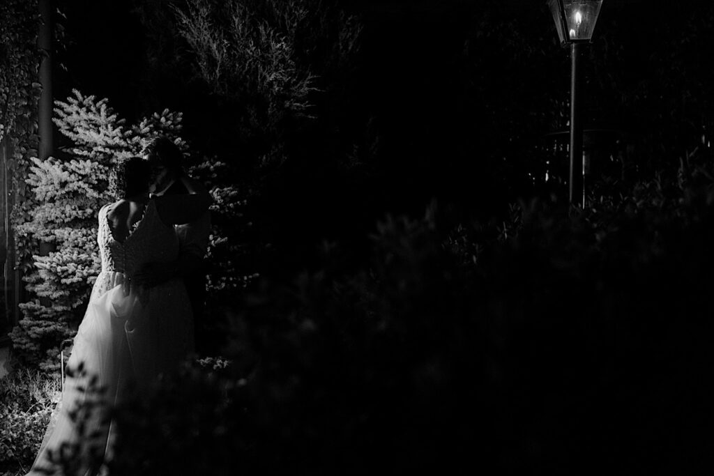 Black and white photo of a bride and groom kissing while outdoors surrounded by nature near their wedding venue The Atrium in Milwaukee