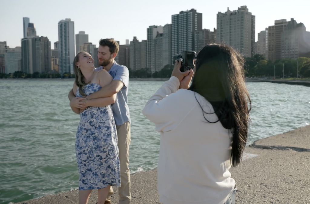 The Chicago wedding photographer, JNA Visuals, takes a picture of a couple standing together at North Avenue Beach with Lake Michigan and the Chicago skyline in the background