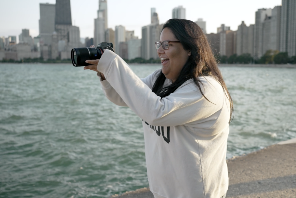 The Chicago wedding photographer, JNA Visuals, smiles while taking a photo at North Avenue Beach with Lake Michigan and the Chicago skyline in the background