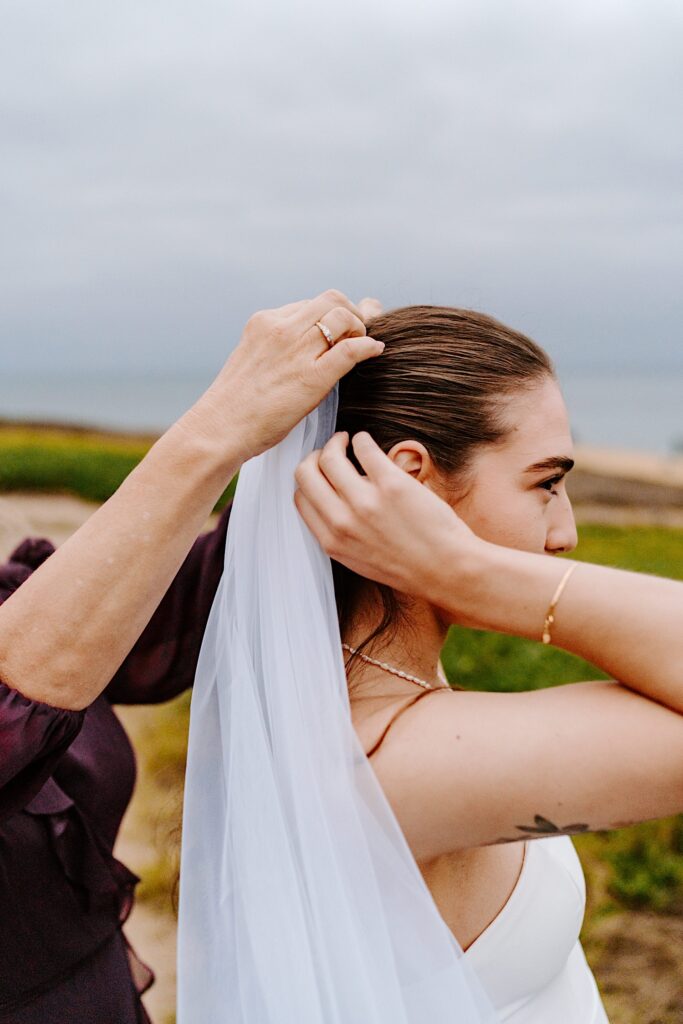 A bride has her veil adjusted by her mother while standing outside on a cloudy day in San Diego