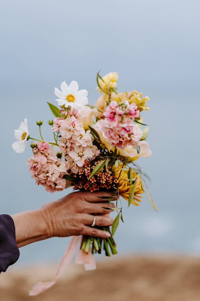 A woman extends a flower bouquet outwards on a cloudy day