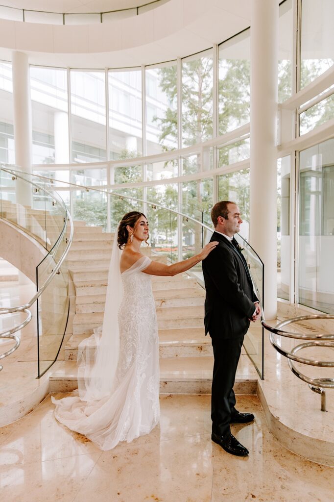 A bride taps the groom on his shoulder to get him to turn around for their first look in the lobby of a hotel