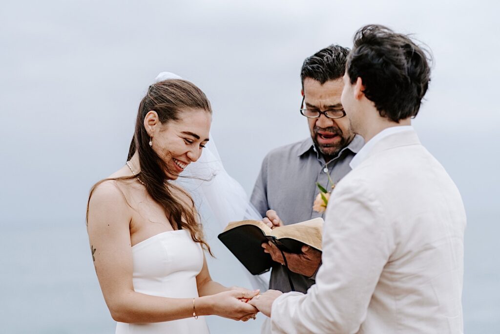 A bride laughs while holding the groom's hands during the ceremony of their destination elopement in San Diego