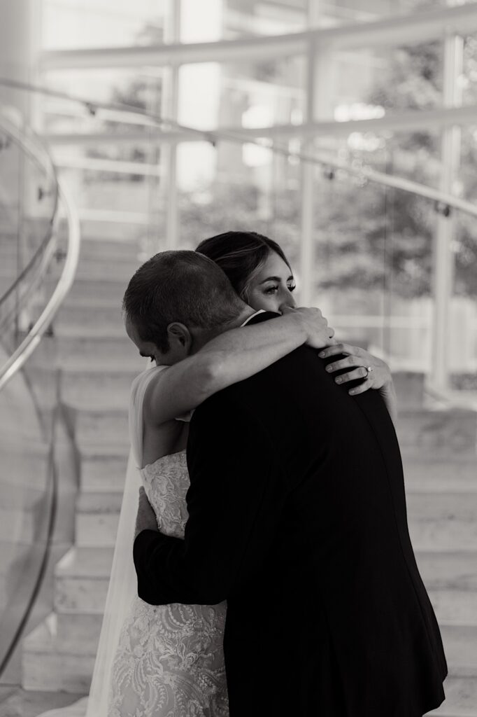 Black and white photo of a bride and groom hugging one another while standing in the lobby of their hotel