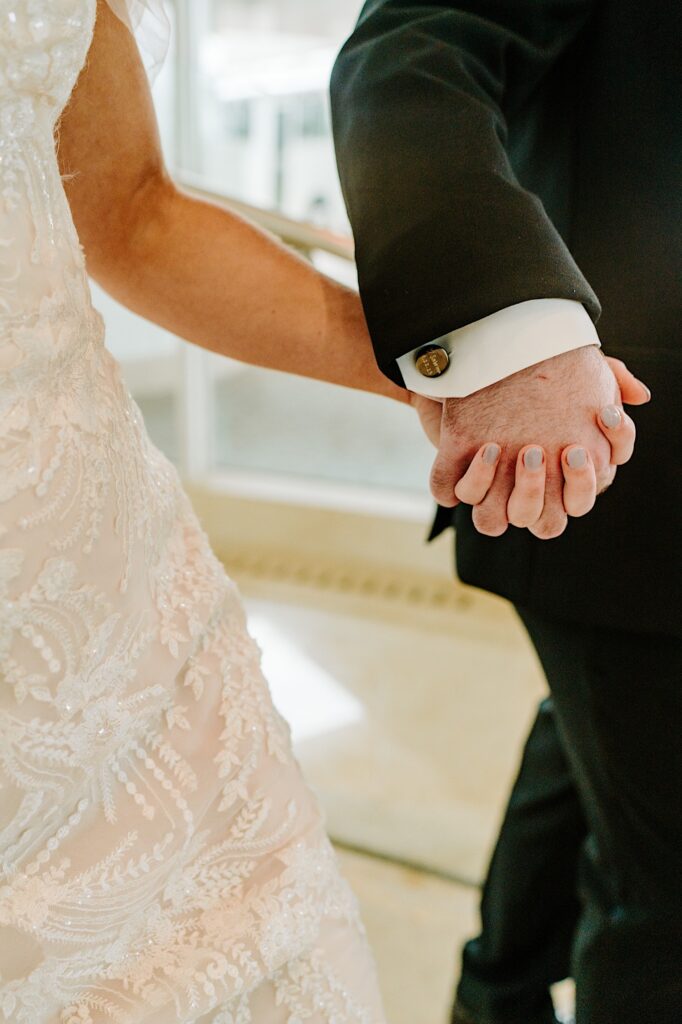 Close up photo of a bride and groom's hands holding one another as they walk next to each other