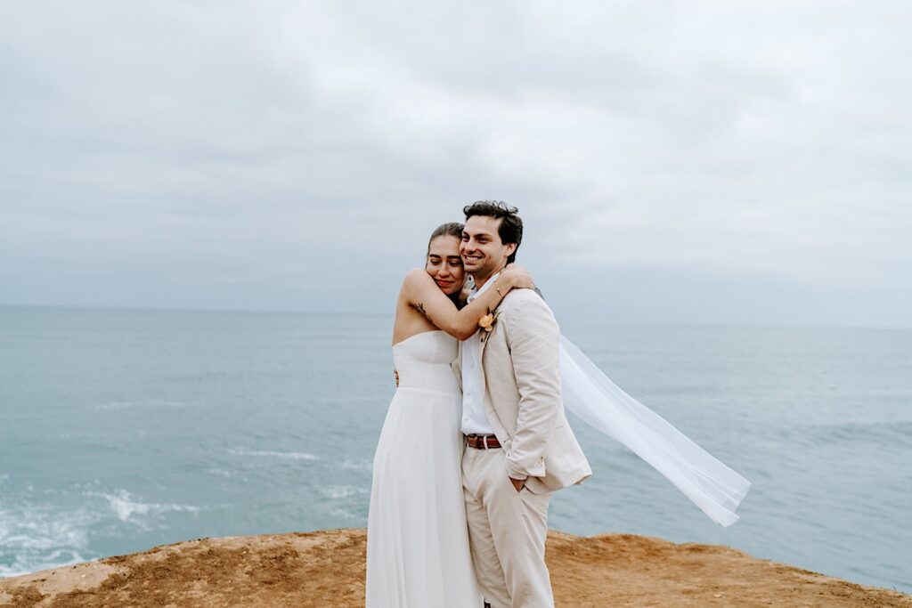 A bride and groom hug after the ceremony of their destination elopement at the cliffs of San Diego