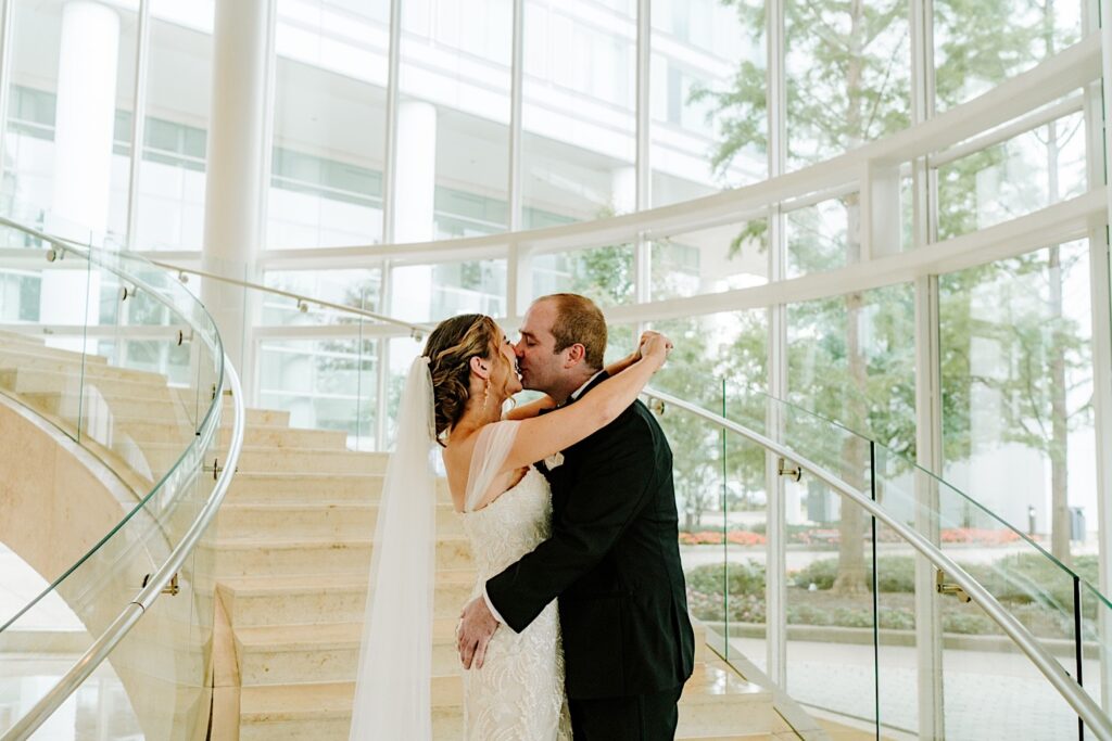 A bride and groom kiss while standing on a set of stairs in the lobby of their hotel before their Chicagoland wedding