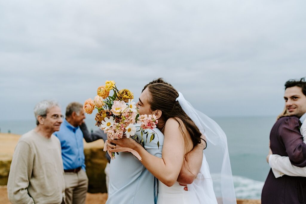 A bride hugs a guest of her destination elopement in San Diego as other guests wait