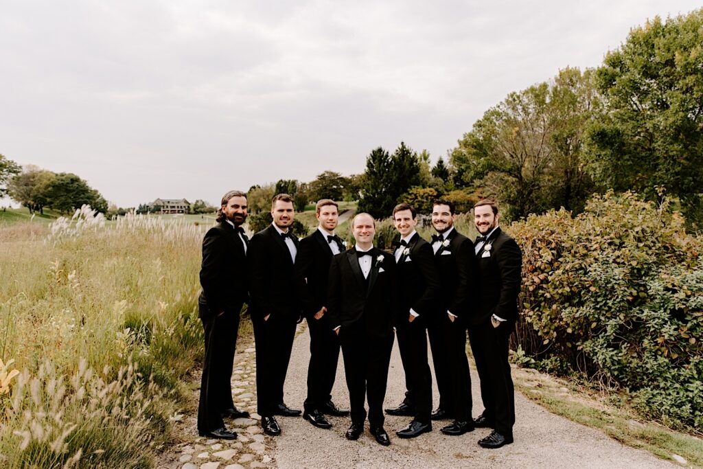 A groom smiles at the camera alongside his 6 groomsmen while at the Makray Golf Club for his wedding in the Chicagoland area