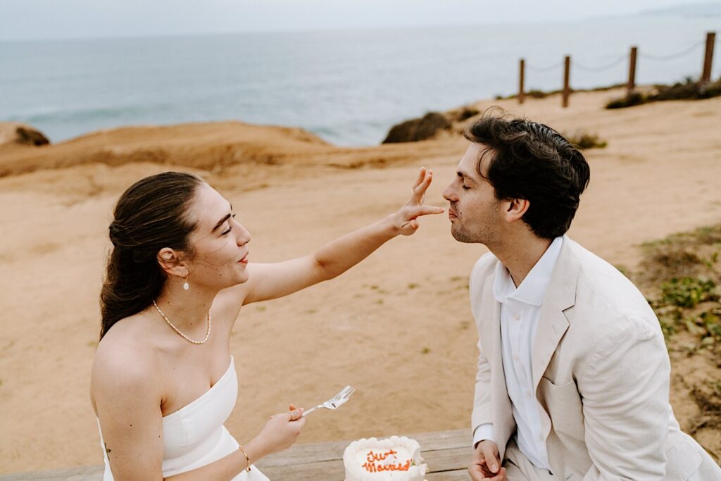 A bride feeds a piece of cake to the groom after the ceremony for their destination elopement in San Diego
