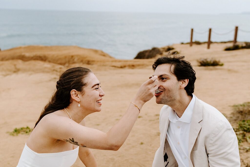 A bride laughs while feeding a piece of cake to the groom after the ceremony of their outdoor destination elopement in San Diego