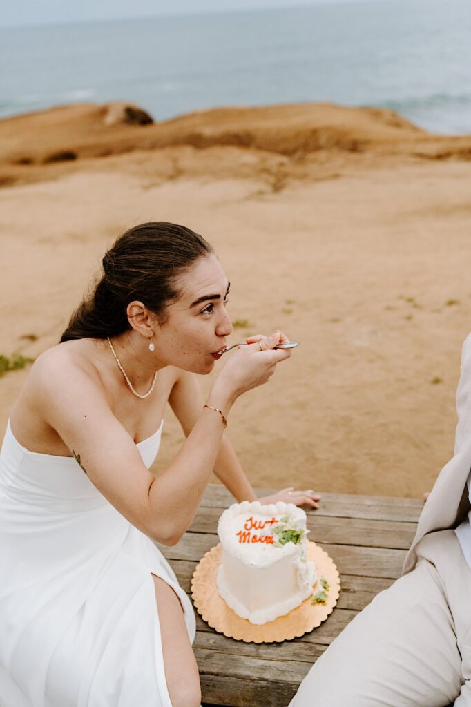 A bride sits on a bench and eats a piece of pistachio cake while on the cliffs of San Diego