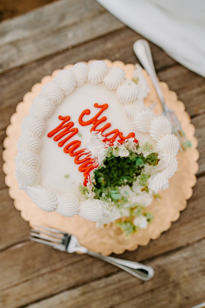 A white heart cake with "Just Married!" written in frosting sits on a bench with some bites taken out of it
