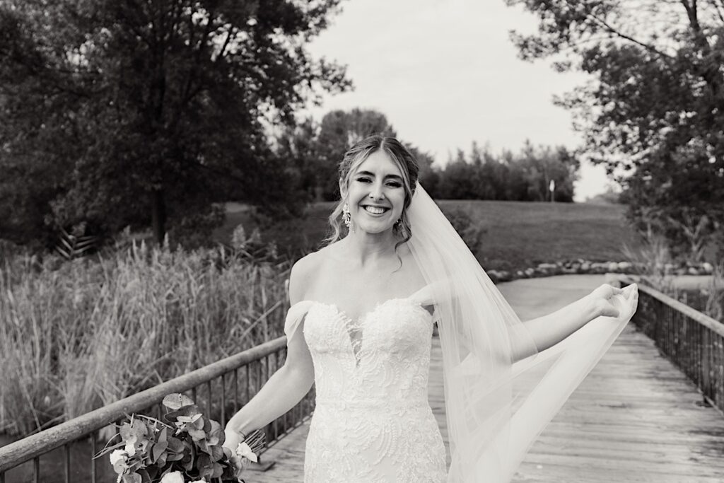 Black and white photo of a bride smiling while walking along a bridge in the Makray Golf Club before her Chicagoland wedding day