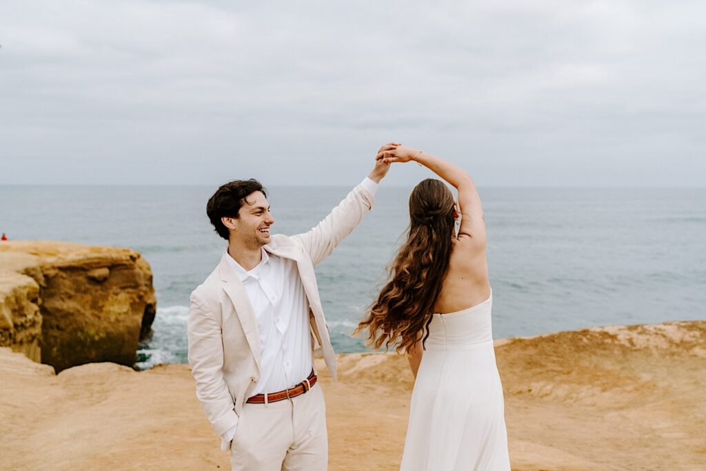 A groom smiles while dancing with the bride at the cliffs in San Diego as the two celebrate their destination elopement