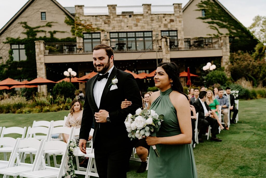 A bridesmaid and groomsman walk down the aisle together at an outdoor wedding ceremony at the Makray Golf Club in the Chicagoland area