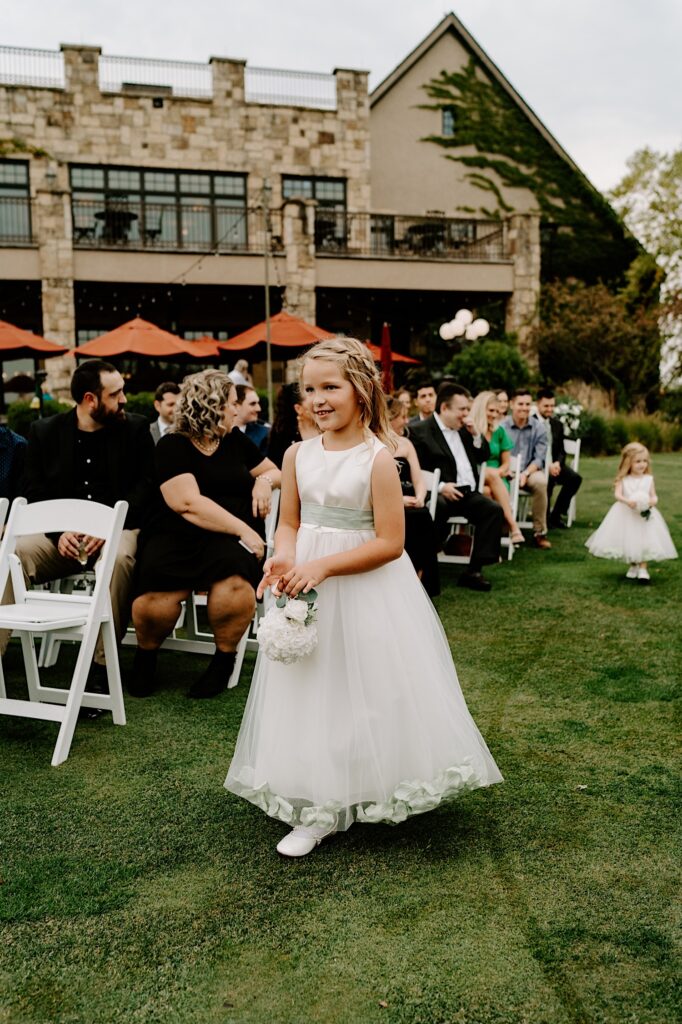 A flower girl walks down the aisle of an outdoor wedding ceremony at the Makray Golf Club
