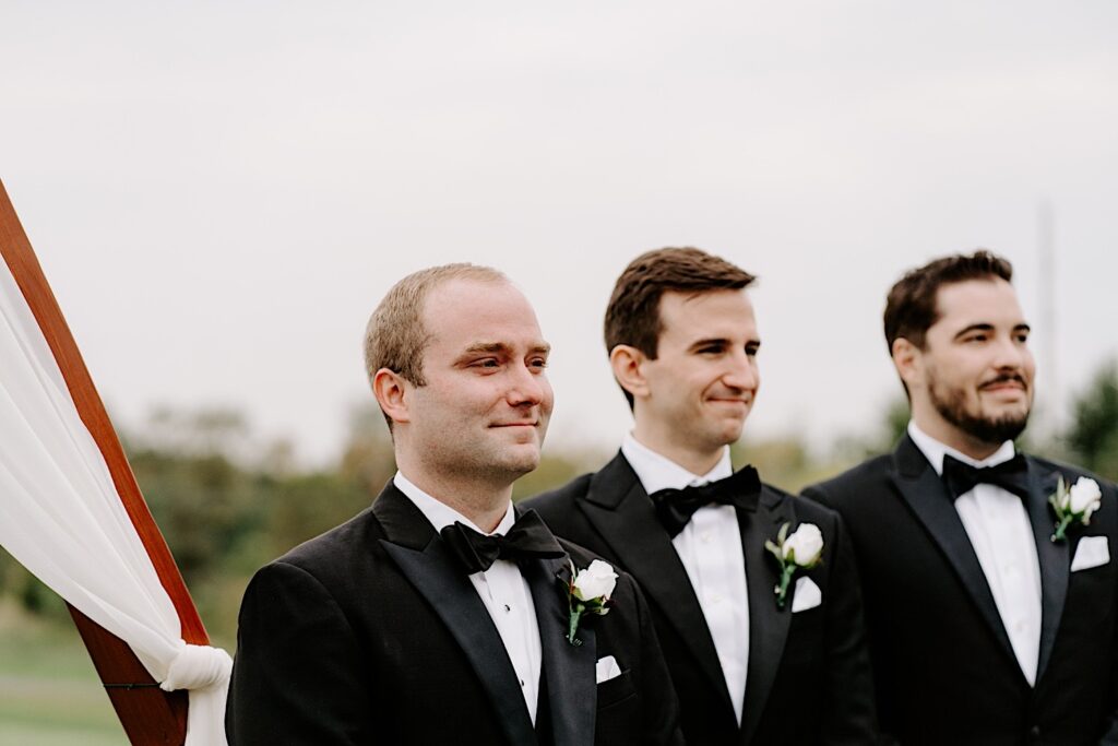 A groom smiles while next to his groomsmen during his outdoor wedding ceremony at the Makray Golf Club in the Chicagoland area