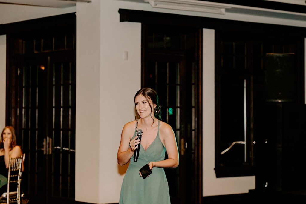 A bridesmaid smiles while standing and giving a speech during an indoor wedding reception at the Makray Golf Club in the Chicagoland area