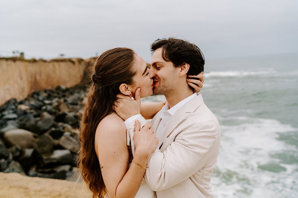 A bride and groom kiss one another while on a beach in San Diego as they celebrate their destination elopement