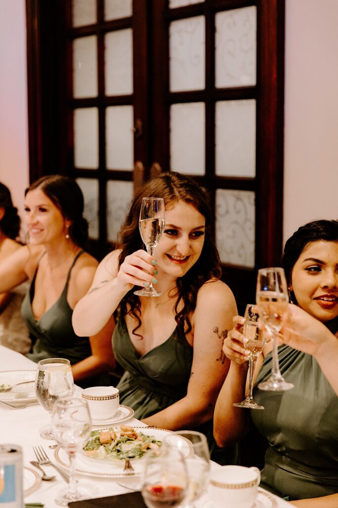 Bridesmaids sit together at a table and raise their glasses for a toast