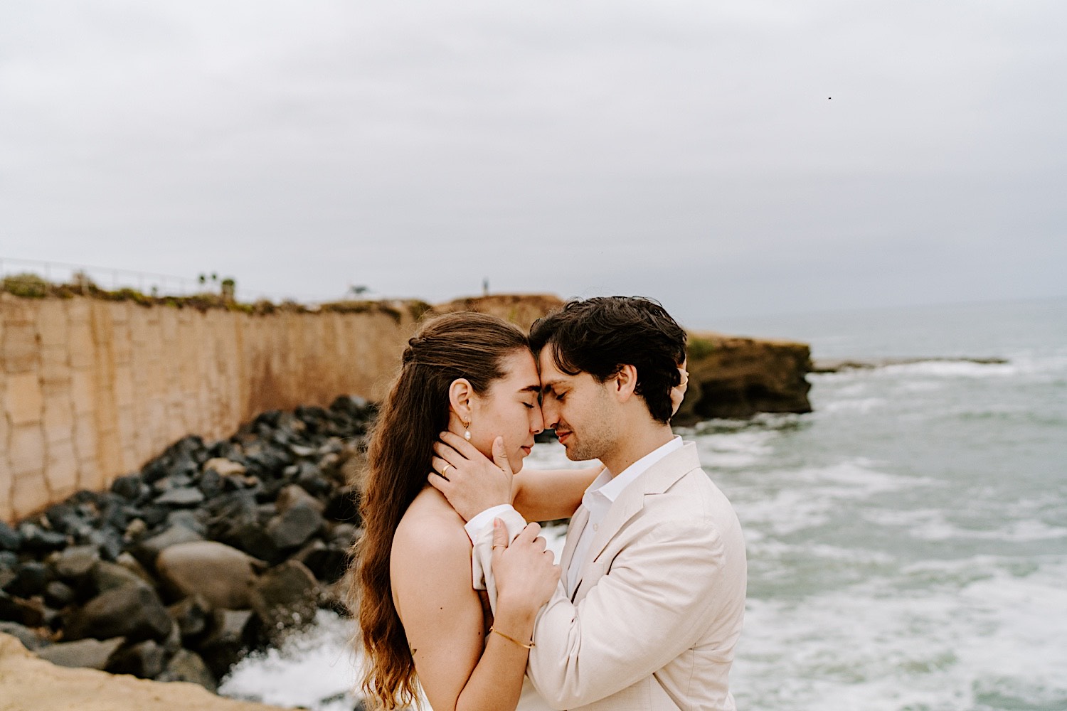 A bride and groom close their eyes and embrace while on a beach in San Diego as they celebrate their destination elopement