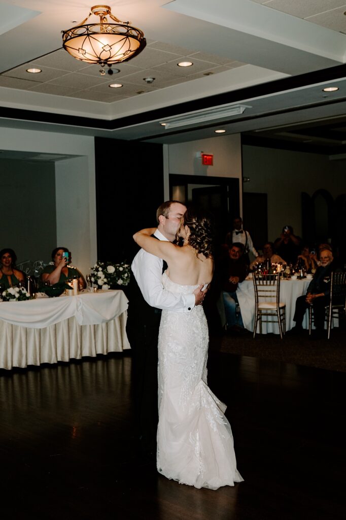 A bride and groom kiss during their first dance at their indoor wedding reception at the Makray Golf Club