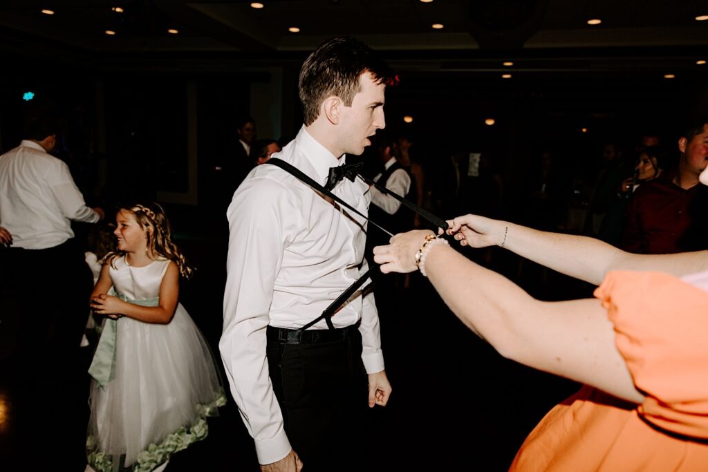 A groomsmen is pulled on the dancefloor by his suspenders during an indoor wedding reception at the Makray Golf Club in the Chicagoland area