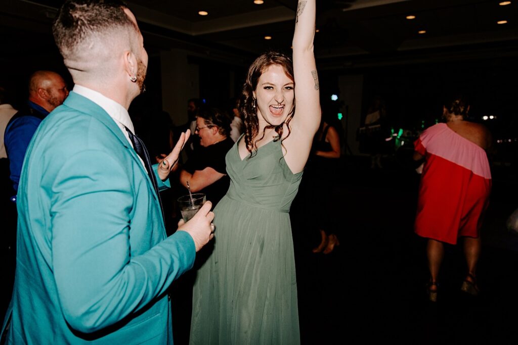 A bridesmaid smiles at the camera and lifts her arm in the air during an indoor wedding reception at the Makray Golf Club in the Chicagoland area