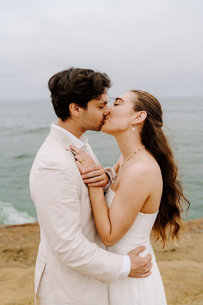 A bride and groom kiss while at the cliffs in San Diego on a cloudy day 