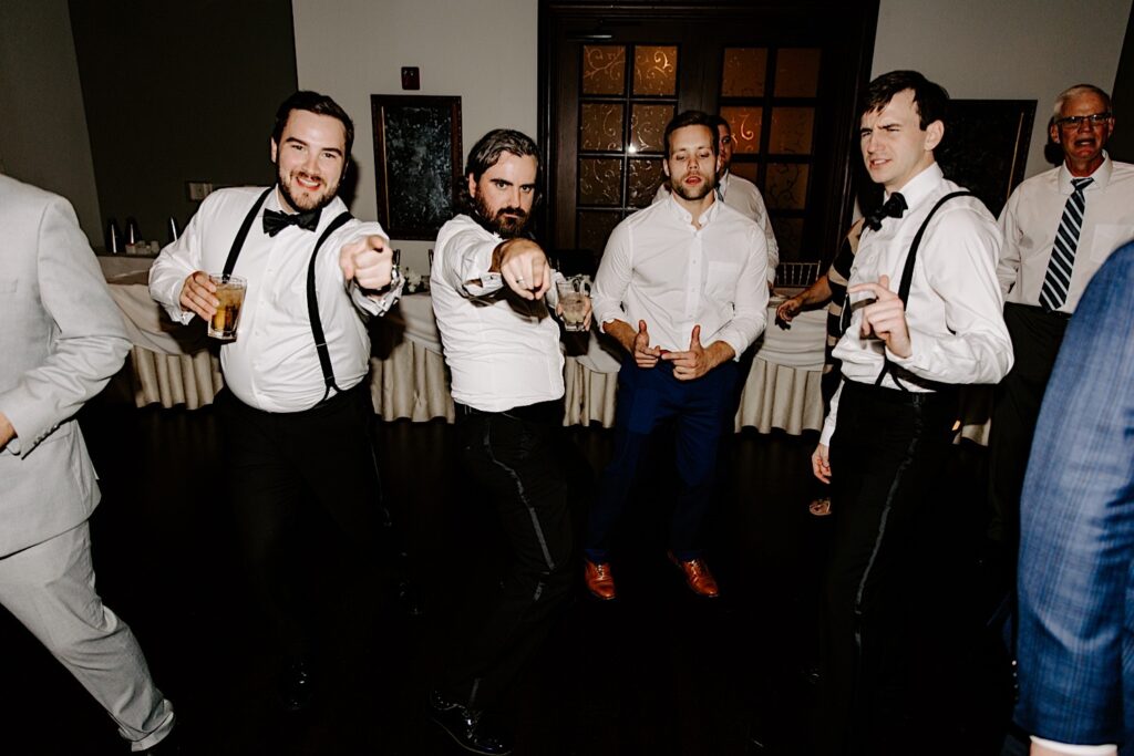 Groomsmen dance together and point at the camera during an indoor wedding reception at the Makray Golf Club in the Chicagoland area