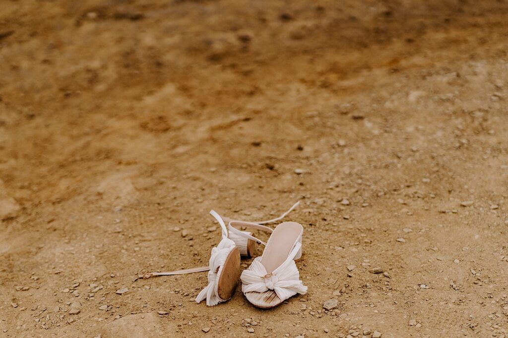 A pair of woman's wedding shoes sit on the ground at the cliffs in San Diego