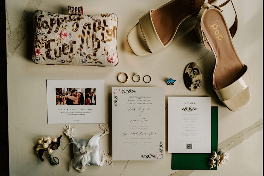 A wedding day flatlay consisting of wedding invites, rings photographs, shoes, and other décor.