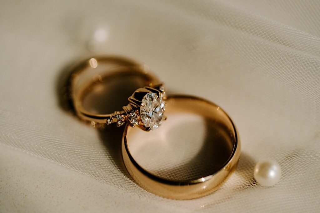 Detail photo of wedding rings resting atop one another on a piece of fabric next to some pearls