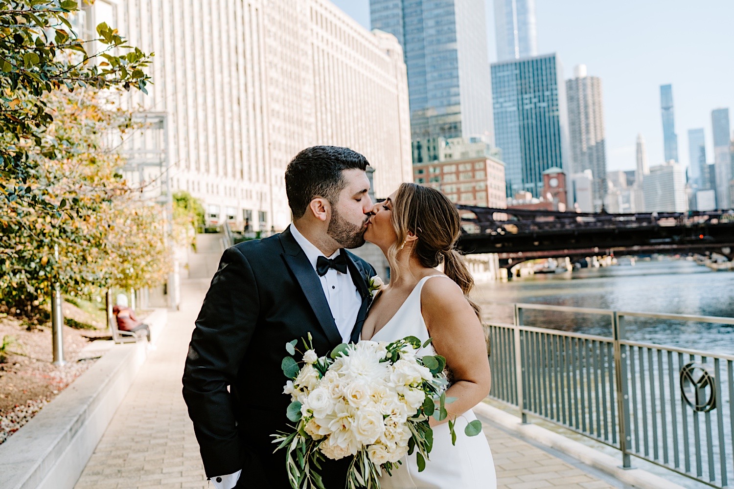 A bride and groom kiss one another while on a walkway next to the Chicago River before their wedding at the Voco Hotel