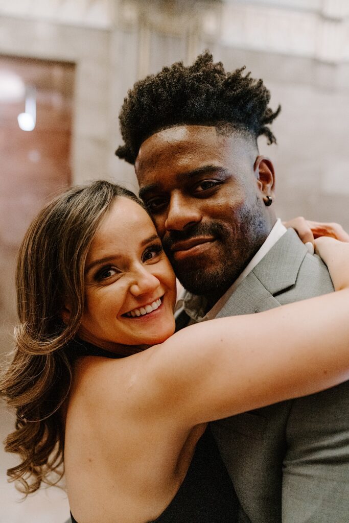 A couple embrace and smile at the camera while inside an art museum