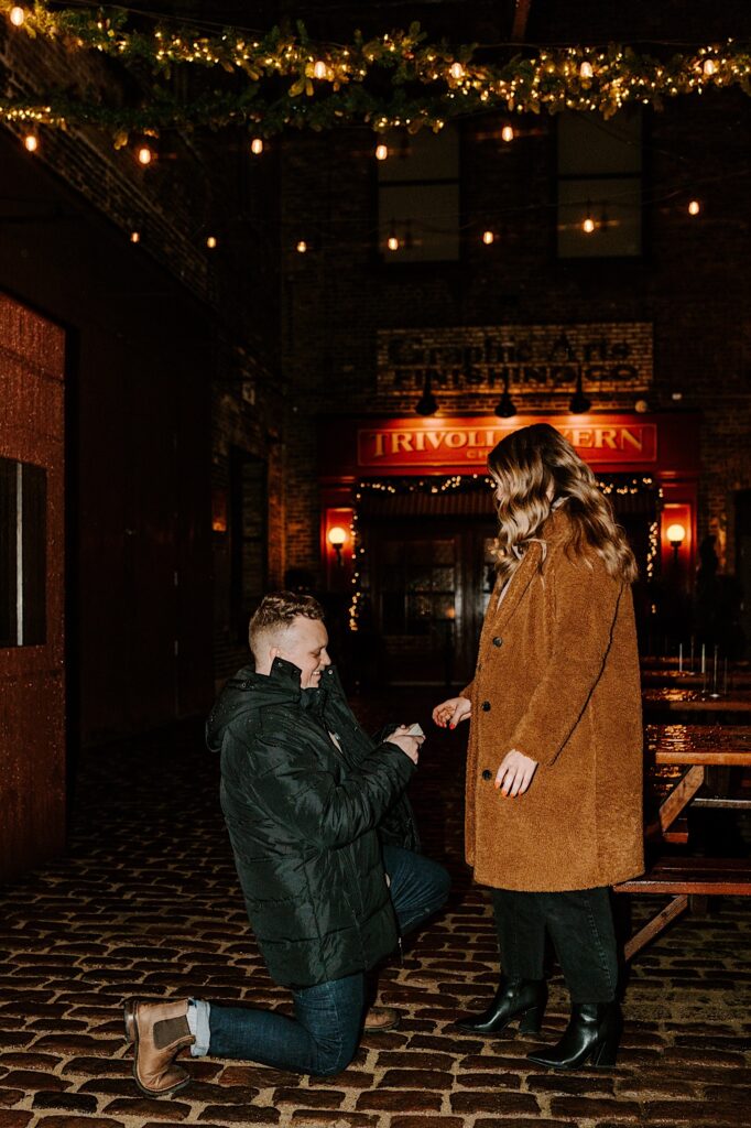 A man gets down on one knee to propose to a woman while outside of the Trivoli Tavern in Chicago