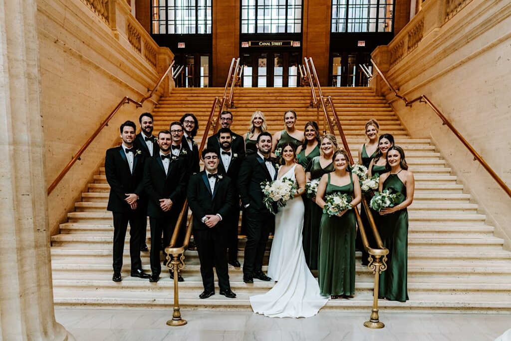 A bride and groom stand with their wedding party members on a staircase inside of Chicago's Union Station for a group portrait