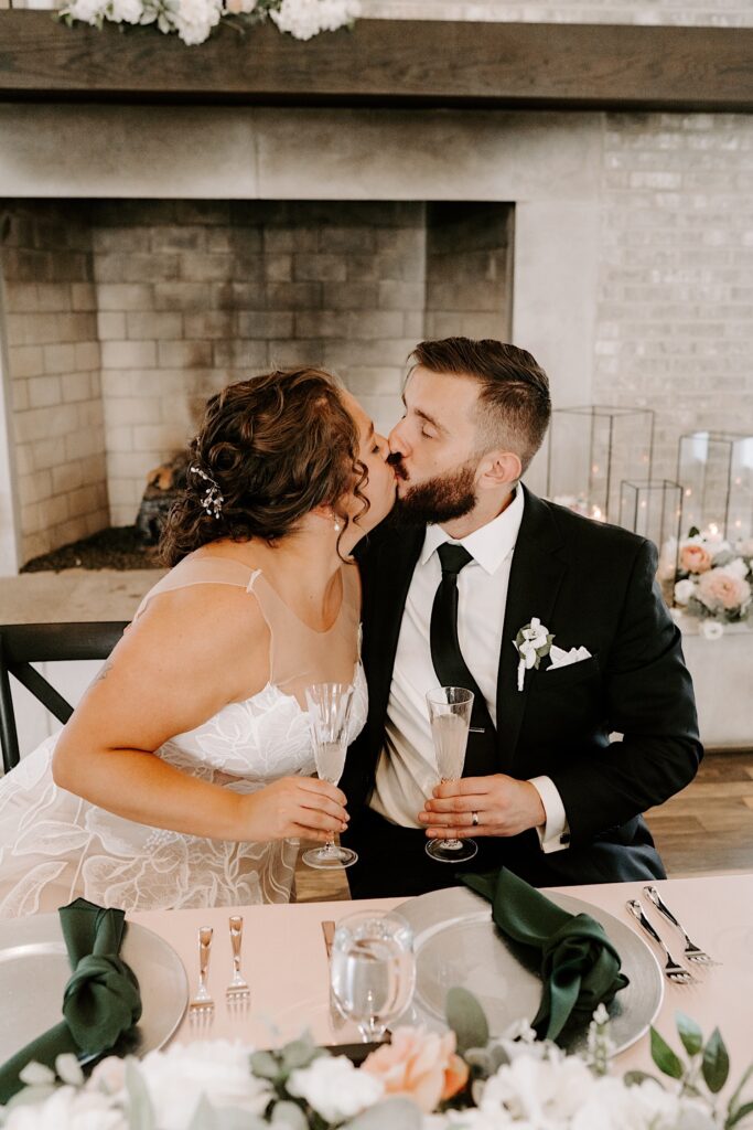 A bride and groom kiss one another while sitting at their sweetheart table