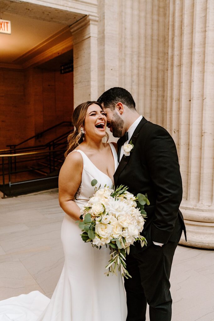 A bride smiles and laughs while the groom tells her a joke while the two are inside Chicago's Union Station