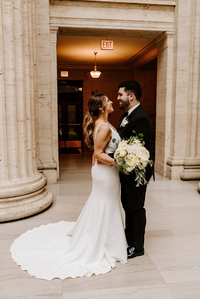 A bride and groom stand facing one another and smile while standing inside of Chicago's Union Station