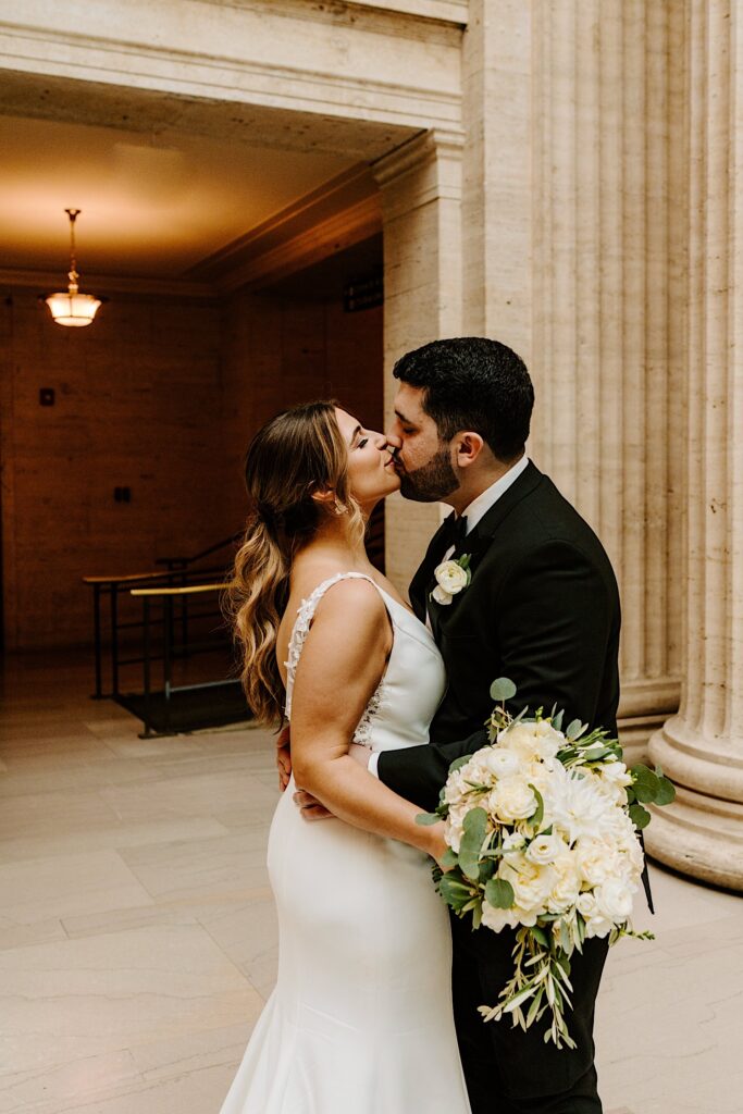 A bride and groom kiss one another while the groom hugs the bride inside of Chicago's Union Station