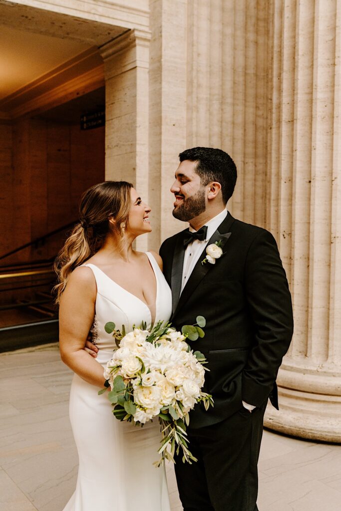 A bride and groom smile at one another while standing side by side inside of Chicago's Union Station