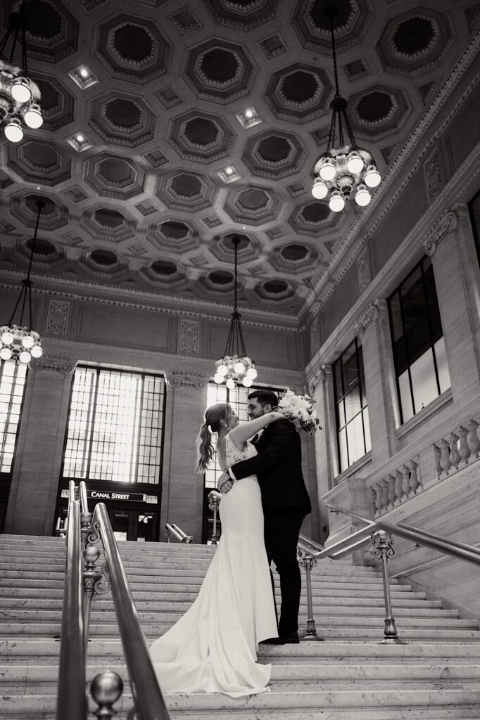 Black and white photo of a bride and groom embracing one another while on a staircase inside of Chicago's Union Station
