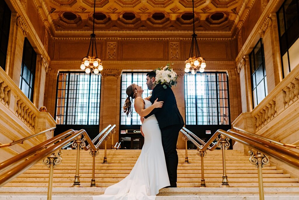 A bride and groom stand on a staircase inside of Chicago's Union Station as the groom leans in for a kiss